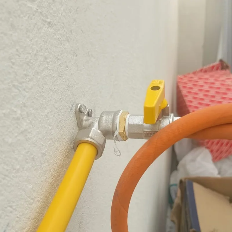 Close-up of a composite gas pipe fitting with a yellow ball valve and orange hose connection