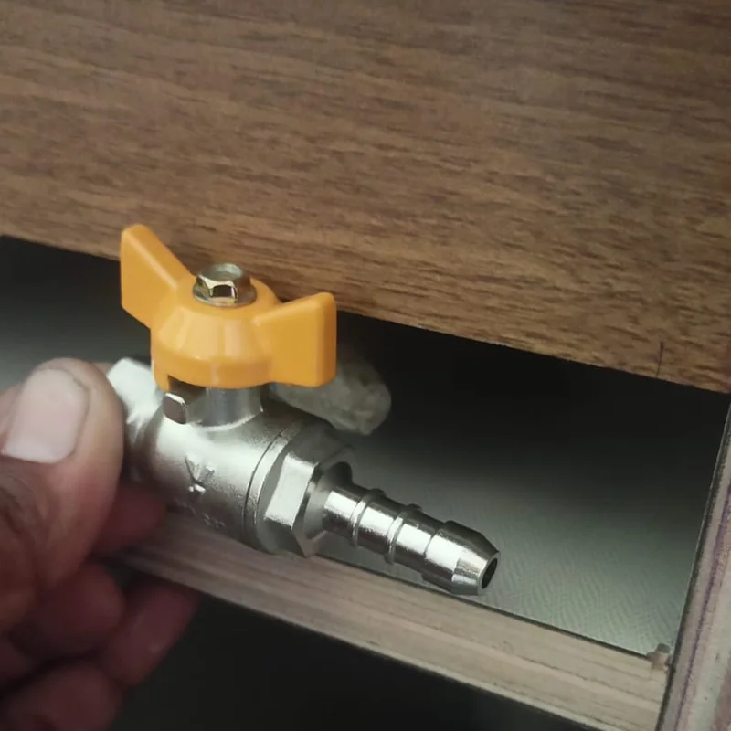 Hand holding a gas pipeline ball valve fitting during installation under a kitchen cabinet