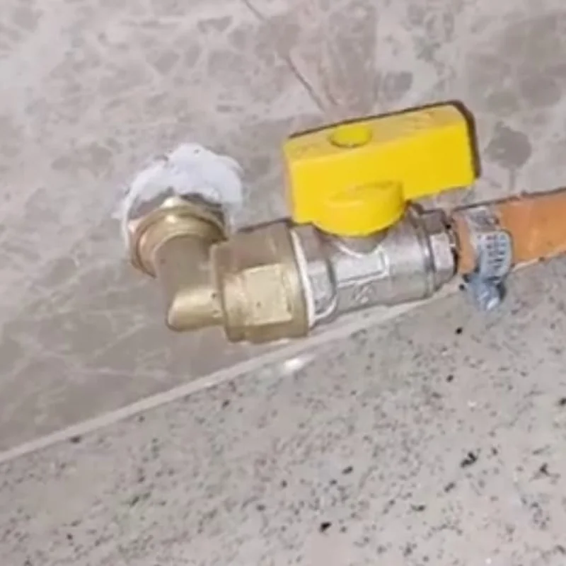 Close-up of a gas ball valve and copper pipe connection mounted on a marble wall