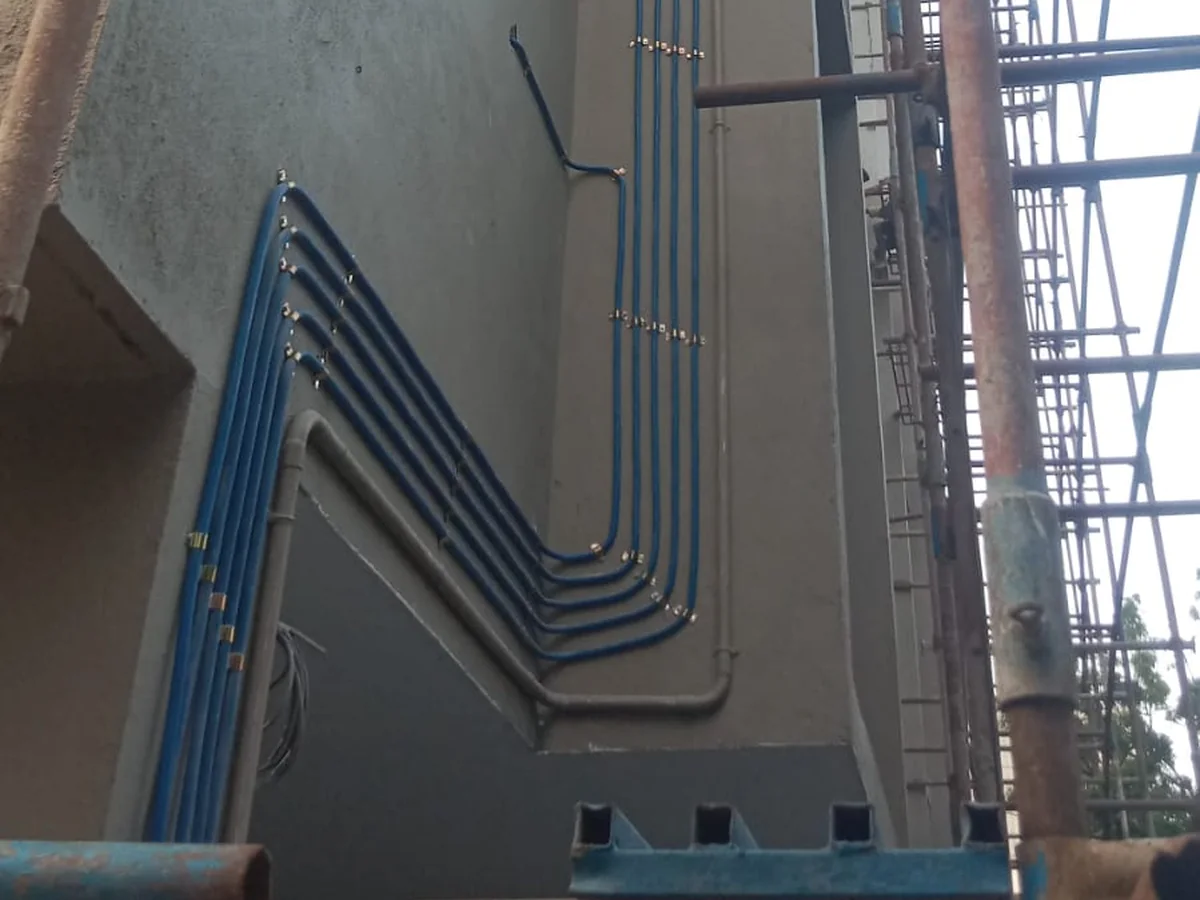 Multiple gas pipeline risers bending across an apartment building exterior during construction, scaffolding visible