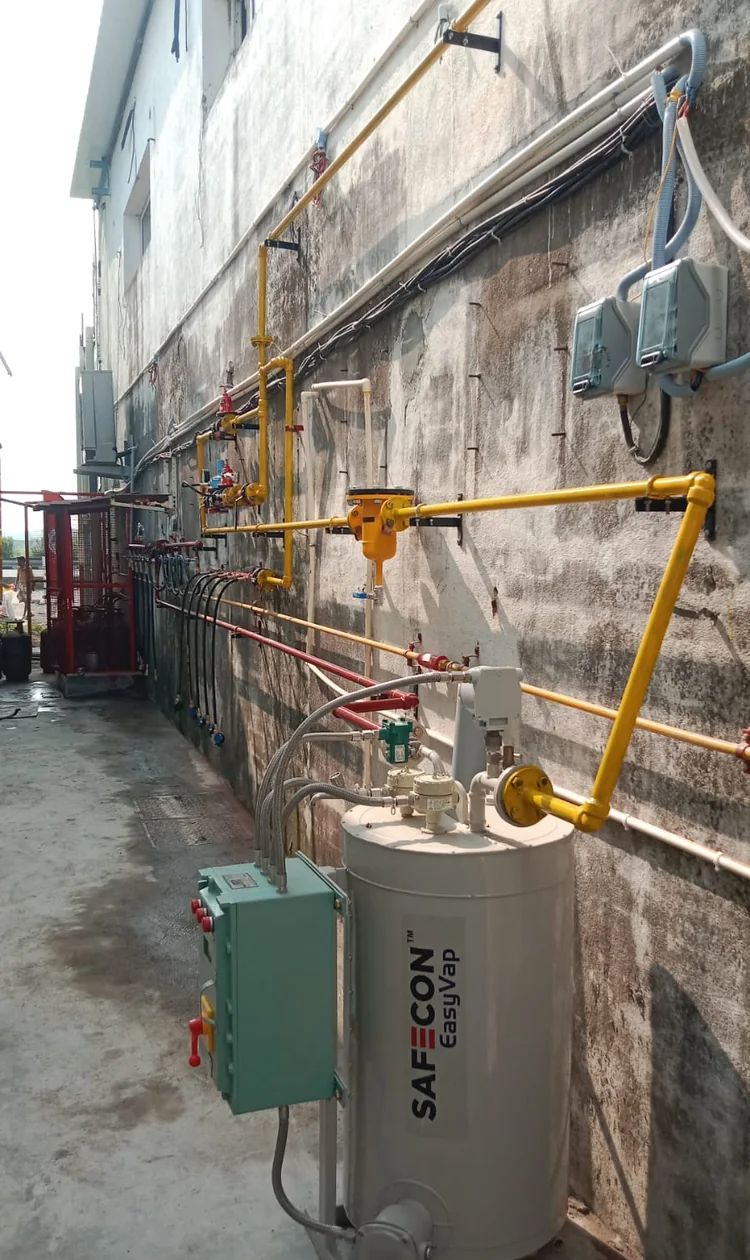 Industrial gas pipeline manifold with a vaporizer and control panel installed along a factory exterior wall